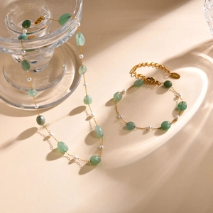 Elegant gold chain jewelry set with green stones and pearls on a textured background