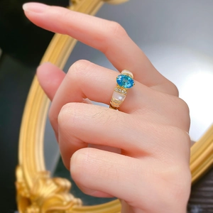 Macro shot of a gold ring with a Paraiba blue gemstone and white enamel shell detail