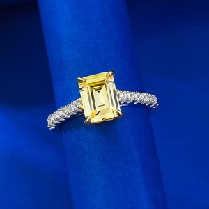 Emerald cut yellow gemstone ring in silver finish with micro-pave diamonds on blue stand