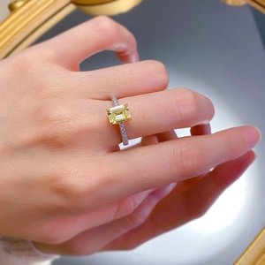 Macro shot of yellow emerald-cut simulated diamond ring with pavé side stones on hand