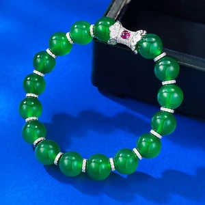 Macro shot of green chalcedony beaded bracelet with silver bow and red gemstone