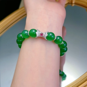 Detail of green agate bead bracelet with a bow pendant and red gemstone on wrist