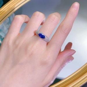 Detail of marquise-cut blue gemstone ring with gold pave diamond band on model's hand