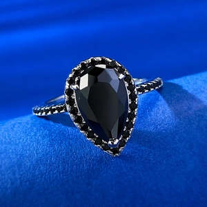 Detailed macro view of pear-cut black zircon ring with halo setting on a blue texture