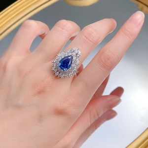 Pear-shaped royal blue stone ring with marquise halo on a reflective mirror surface
