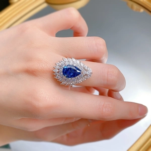 Close-up of a pear-shaped royal blue gem ring with marquise halo on female finger