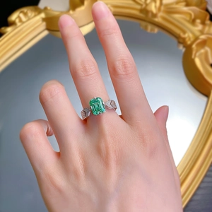 Detailed view of an emerald-cut green gemstone ring with pavé diamonds on a silver band