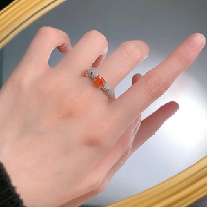 Detailed view of an oval orange gemstone ring with pave diamonds on a model's hand