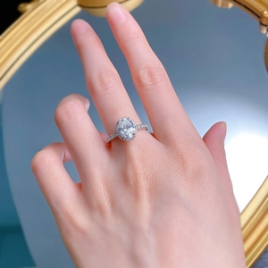 Detailed view of an oval-cut white stone ring with pavé setting on a hand