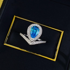 Detailed macro view of pear-cut blue gemstone ring in V-shaped diamond halo setting
