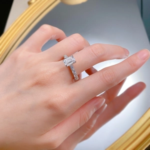 Macro shot of an emerald-cut silver ring with paved side diamonds worn on a finger