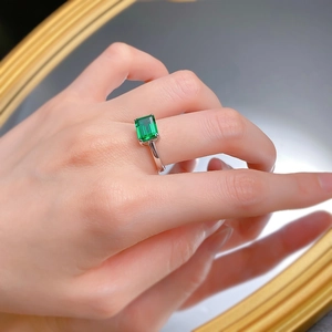 Detailed close-up of a emerald-cut green gemstone ring worn with a mirror reflection