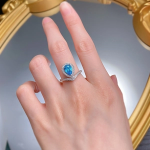 Macro view of pear-cut blue gemstone ring with V-shaped diamond band on model