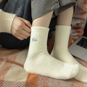 Close-up of warm cream fuzzy socks with cute rabbit embroidery on cozy blanket