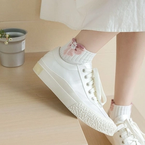 White mid-tube socks with pink flower pattern paired with canvas shoes on wooden stairs