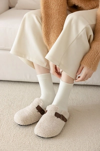 Detail of beige sherpa fleece mule slippers featuring brown leather strap and buckle closure