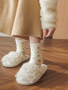 Close-up of cozy mink velvet socks with colorful dots and plush slippers on wood floor