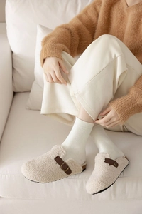 Close-up of beige faux shearling mule slippers with brown buckle strap for home wear