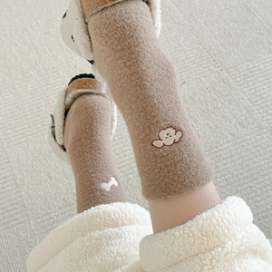 Close-up of thick caramel plush socks with cute white embroidery on soft rug