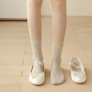 Nahaufnahme weißer Satin-Ballerinas mit Schleife und beigen gerippten Socken auf Holz