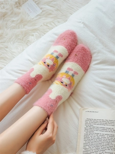 Close-up of plush pink striped socks with cartoon girl design on soft white rug