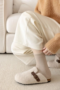 Detail of warm beige sherpa slippers with brown leather buckle and ribbed knit socks