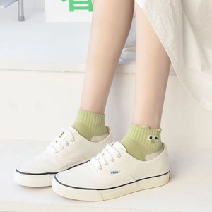 Detail of light green cotton socks with cartoon monster embroidery worn with white sneakers