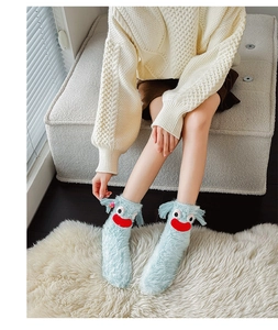 Close-up of fuzzy light blue monster socks with big eyes on soft white carpet