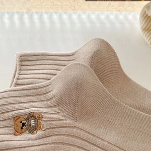 Gros plan d'une chaussette en coton avoine avec broderie ours et texture côtelée