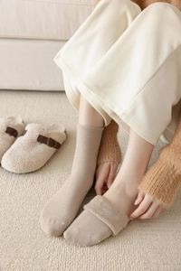 Close-up of thick ribbed knit crew socks in oatmeal color paired with cozy slippers