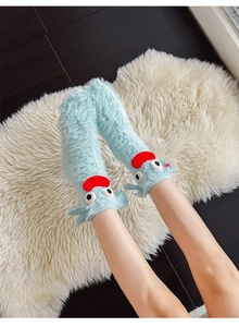 Close-up of light blue fuzzy monster socks with big eyes and red lips on white rug
