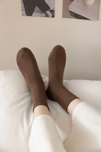 Close-up detail of soft brown thick crew socks for women resting on a white cushion
