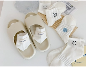 Close-up of white knitted crew socks with embroidered smiley face patterns and branding