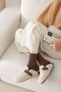 Cozy home lifestyle shot of off-white faux fur mules with brown leather strap detail