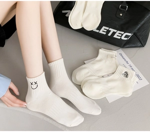 Detail of white cotton crew socks featuring smiley face and bear embroidery with ribbed cuffs