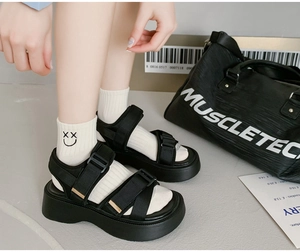 Close-up of black platform sandals with double straps and smiley face socks on a model