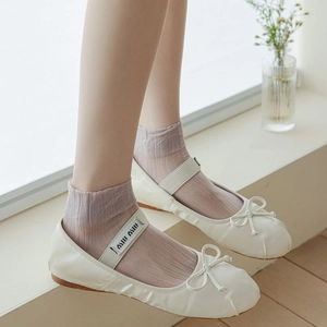 Close-up of white ballet flats with bow and branded elastic strap paired with purple socks