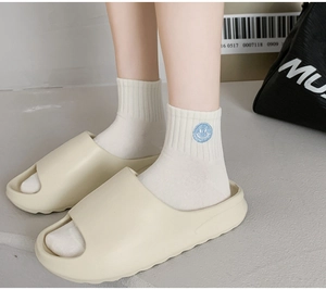 Detail of white cotton sports socks with blue embroidered smiley face and beige EVA slides