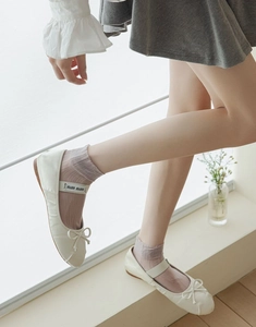 Close-up of beige ballet flats with bow and logo strap paired with thin pink socks
