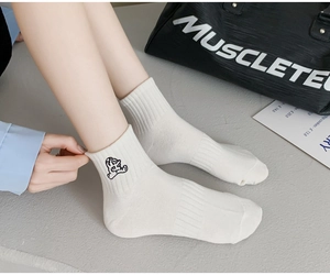 Close-up of white cotton crew socks featuring a minimalist black cartoon embroidery detail