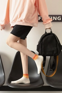 Detail of white cotton ankle sock with orange stripes paired with a black canvas backpack