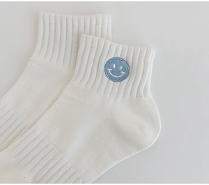 Detail of white cotton mid-tube socks with light blue embroidered smiley face logo