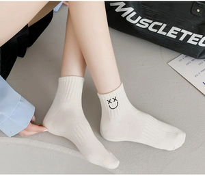 Detail of white cotton crew socks with black embroidered smiley face on ribbed cuff
