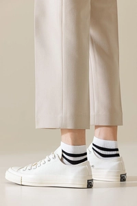 Close-up of classic white canvas low-top sneaker with striped socks and beige trousers