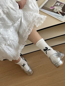 Close-up of white cotton socks featuring black bow embroidery and elegant lace dress detail