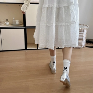 Close-up of white cotton socks with black bow embroidery and silver Mary Jane shoes