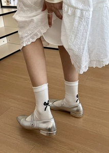 Detail of white cotton socks with black bow embroidery and silver Mary Jane shoes
