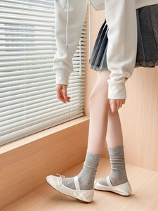 Detail of grey ribbed knit crew socks paired with white ballet flats and bow decoration