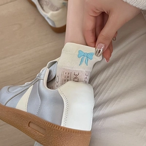 Close-up of mesh socks featuring a blue bow embroidery detail and satin panel sneakers