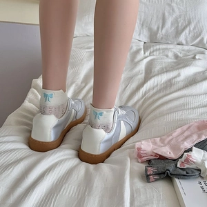 Detail of white mesh socks with a blue bow embroidery paired with casual sneakers